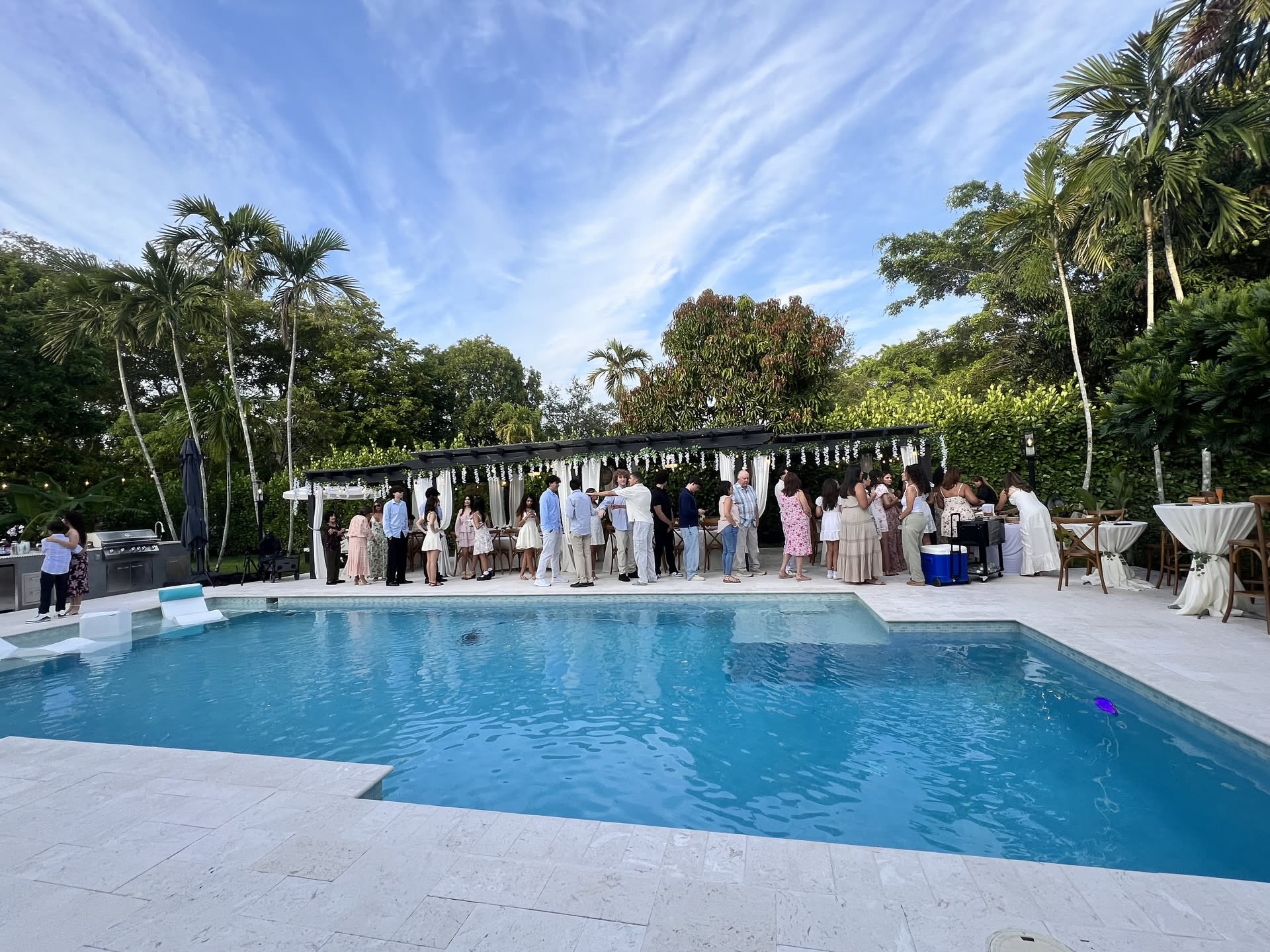 Miami backyard pool party at golden hour with pergola, cocktail bar, and guests gathered poolside